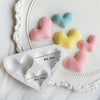 A silicone mold set featuring heart shapes in pink, yellow, and blue colors, displayed on a white plate.