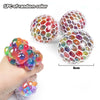 A hand holds a cluster of colorful, translucent stress relief balls with mesh netting alongside two larger spheres.