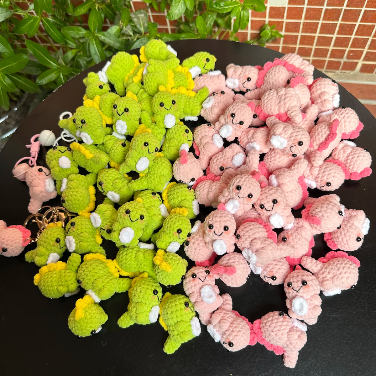 A pile of handmade crochet dinosaur keychains in various shades of green and pink.