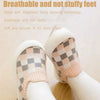 A pair of soft pink and gray plaid slip-on toddler shoes for baby's feet shown on a person's foot.