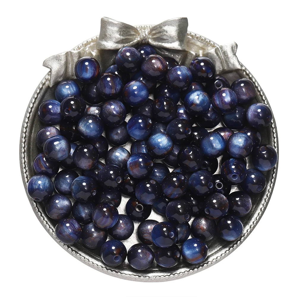 A pile of dark blue glitter cat eye resin beads in a silver-toned dish for jewelry making