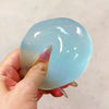A hand holds a translucent light blue squishy stress relief toy with a smooth, rounded shape.