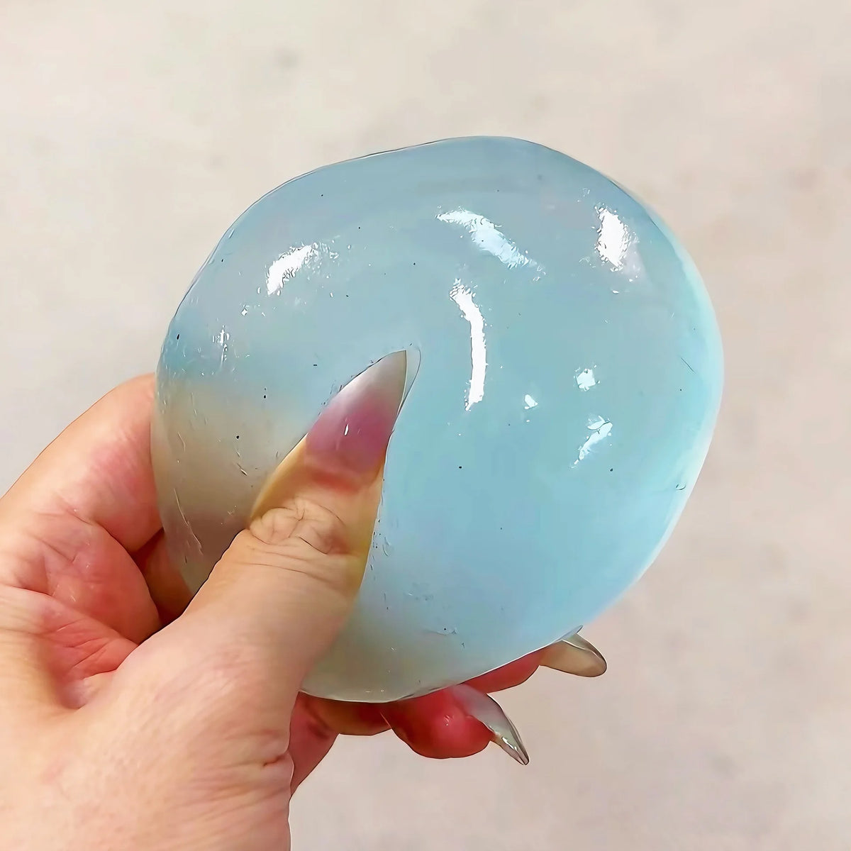 A hand holds a translucent light blue squishy stress relief toy with a smooth, rounded shape.