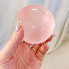 A hand holds a pink, translucent squeeze ball made of coconut oil for stress relief.