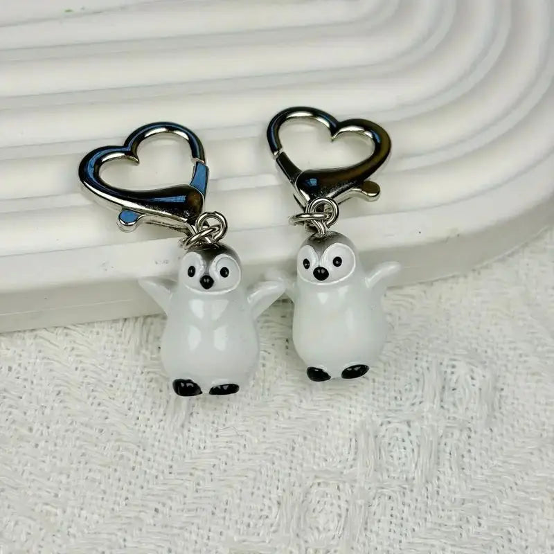 A set of two ceramic penguin heart keychains with silver clasps displayed on a white surface.