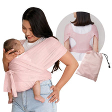 A woman is using an X-shaped baby sling carrier in pink to hold a baby, with a matching pink fabric bag nearby.