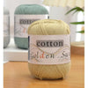 A ball of light beige cotton knitting yarn labeled Golden Sun sits on a wooden surface.