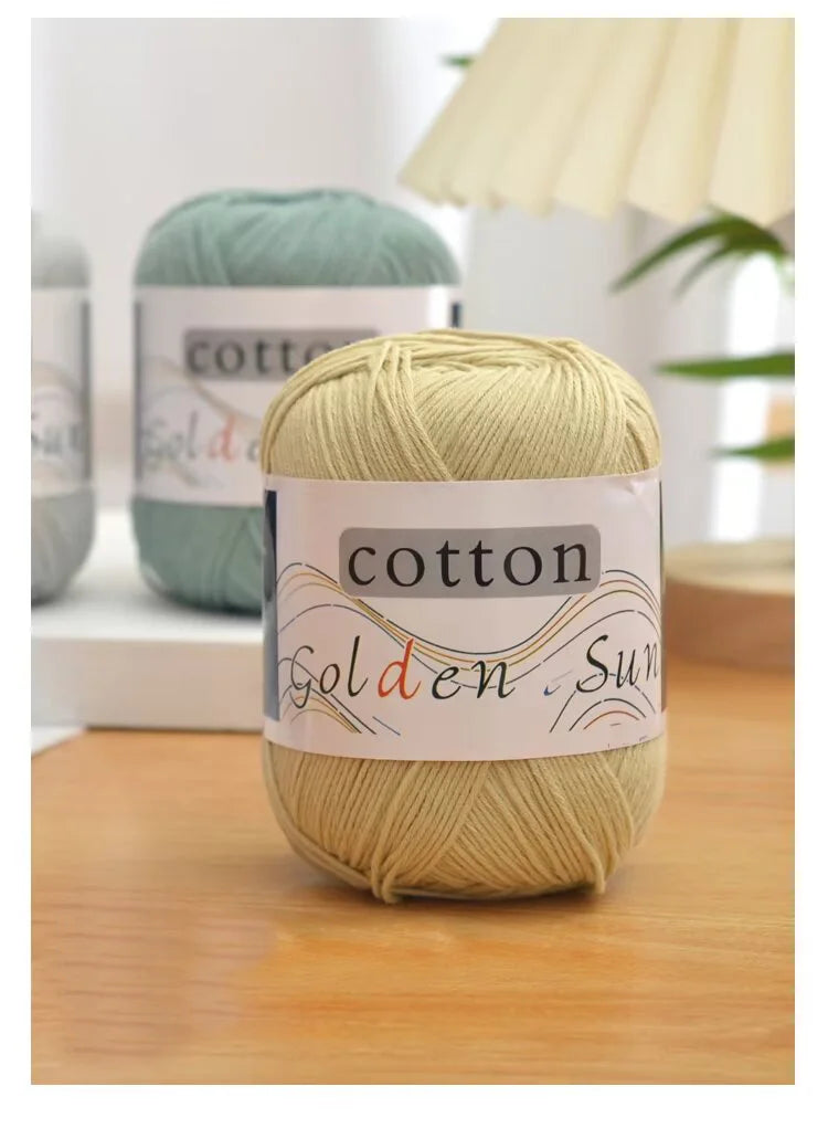 A ball of light beige cotton knitting yarn labeled Golden Sun sits on a wooden surface.