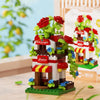 A miniature building set featuring a house and windmill structure with red roses and green foliage.
