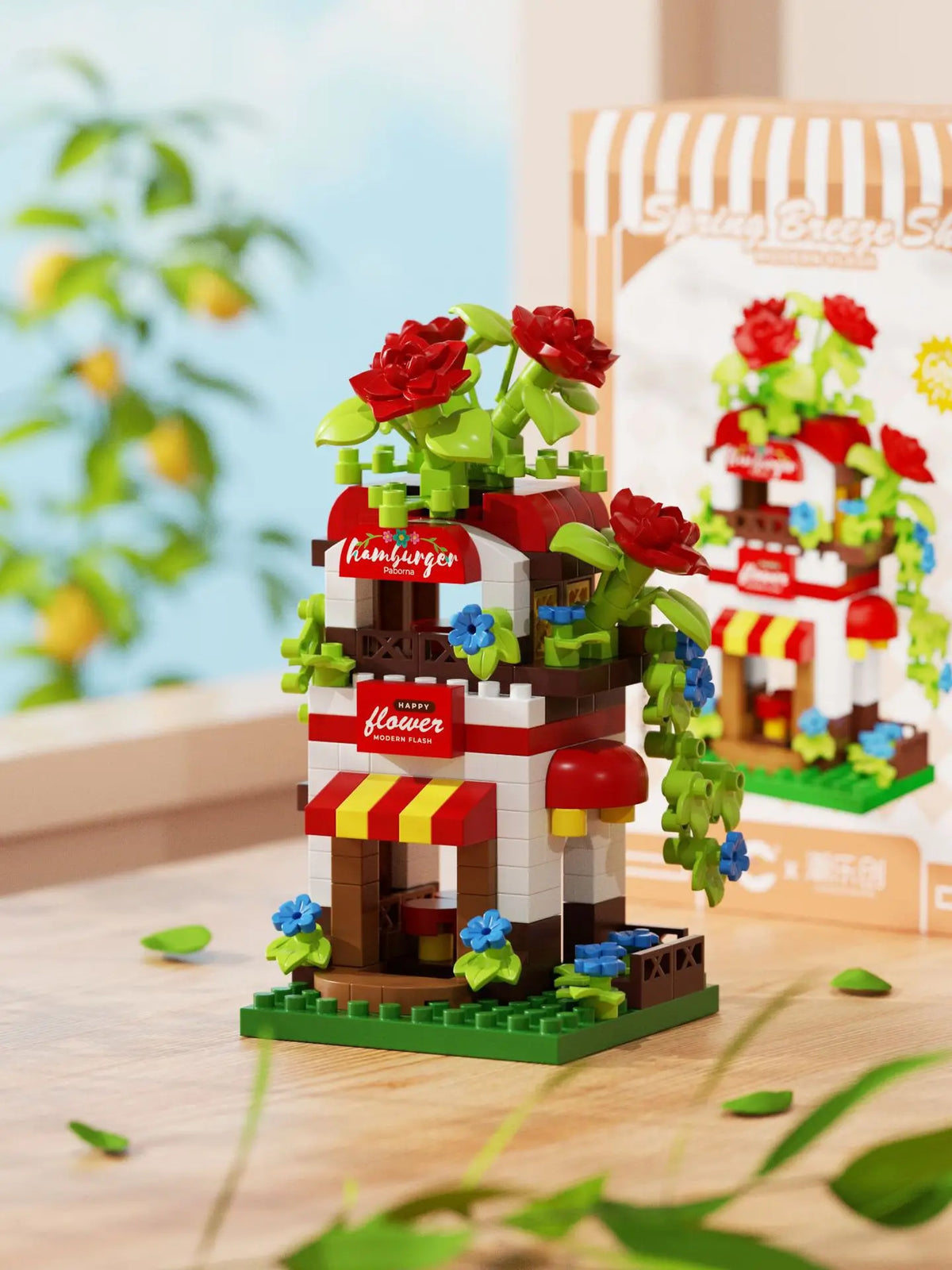 A miniature building set featuring a house and windmill structure with red roses and green foliage.