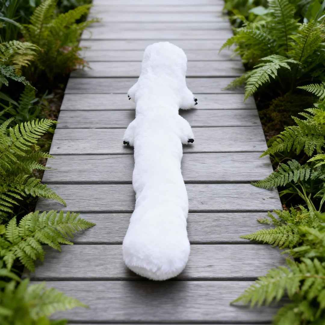 A white anime witch hat plush toy lying on a wooden path surrounded by green foliage.