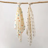 A set of two white baby gauze swaddle blankets tied on a wooden branch.