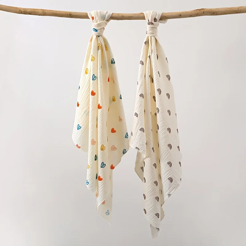 A set of two white baby gauze swaddle blankets tied on a wooden branch.