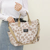 A woman holds a beige floral canvas tote bag with multiple pockets against a light background.