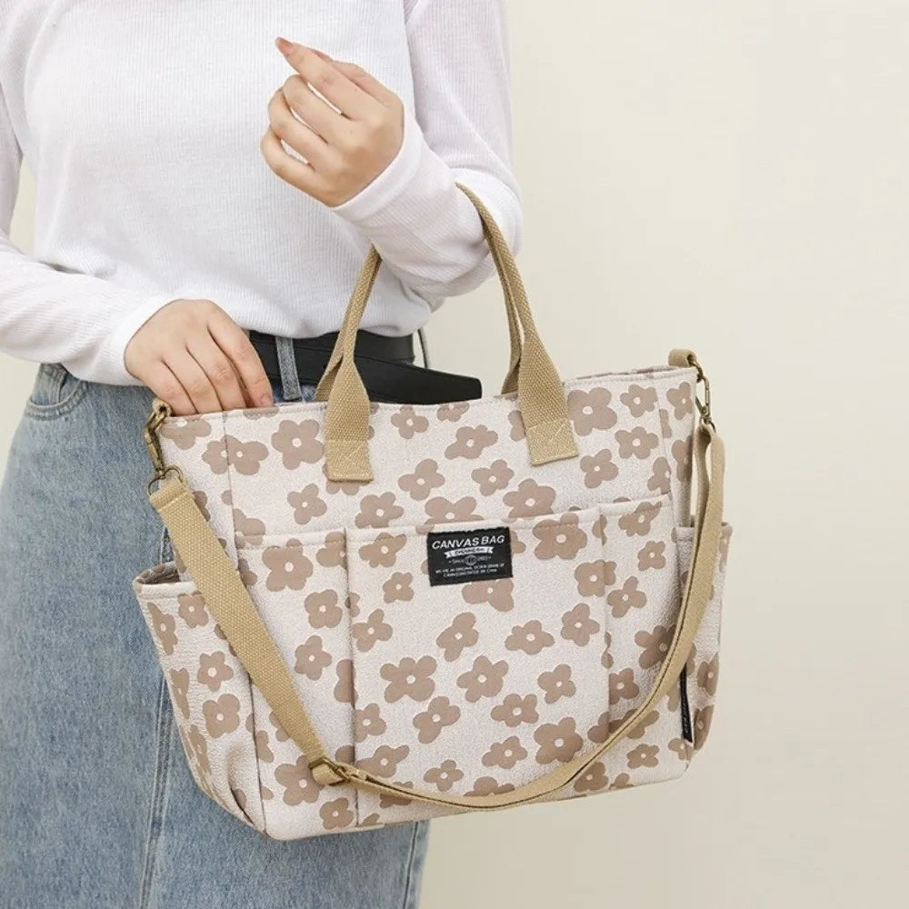 A woman holds a beige floral canvas tote bag with multiple pockets against a light background.