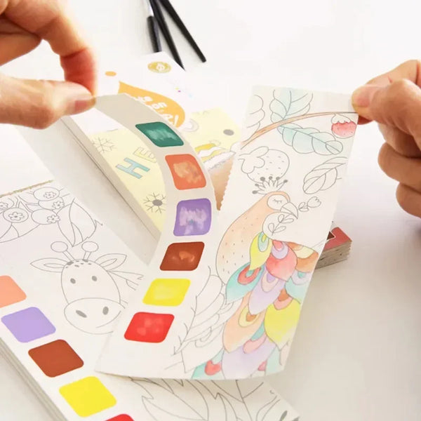 Manos sostienen un libro de acuarelas portátil para niños con paletas de colores e ilustraciones.