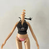 A fashion doll with light skin, wearing a dark patterned top and pink panties, posing with her head tilted back.