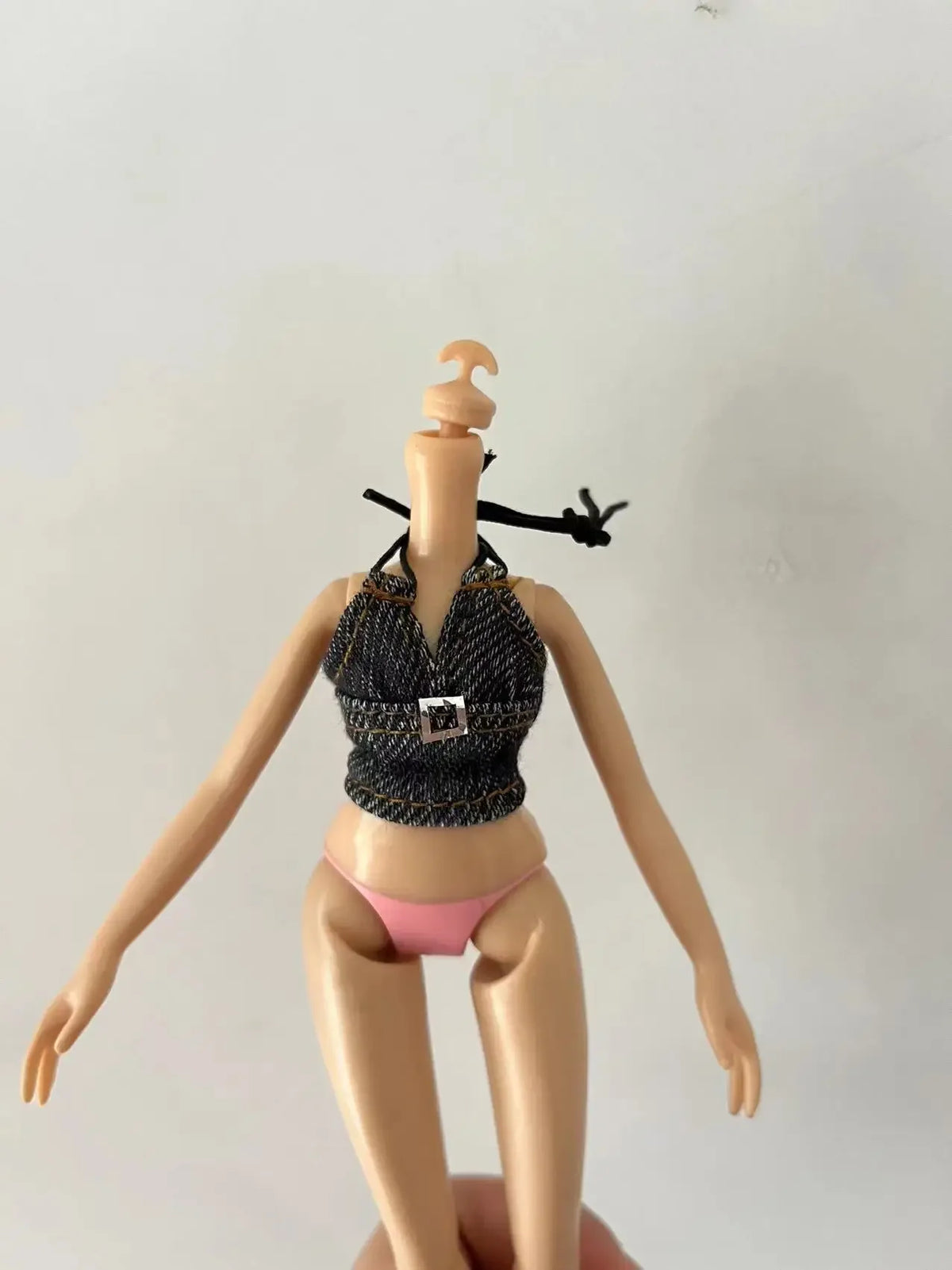 A fashion doll with light skin, wearing a dark patterned top and pink panties, posing with her head tilted back.