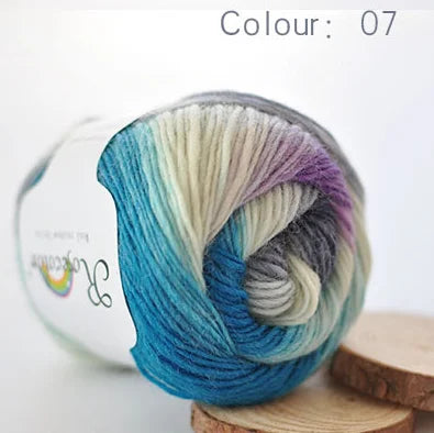 A ball of hand-dyed merino wool yarn in shades of blue, green, and purple is shown on a wooden surface.