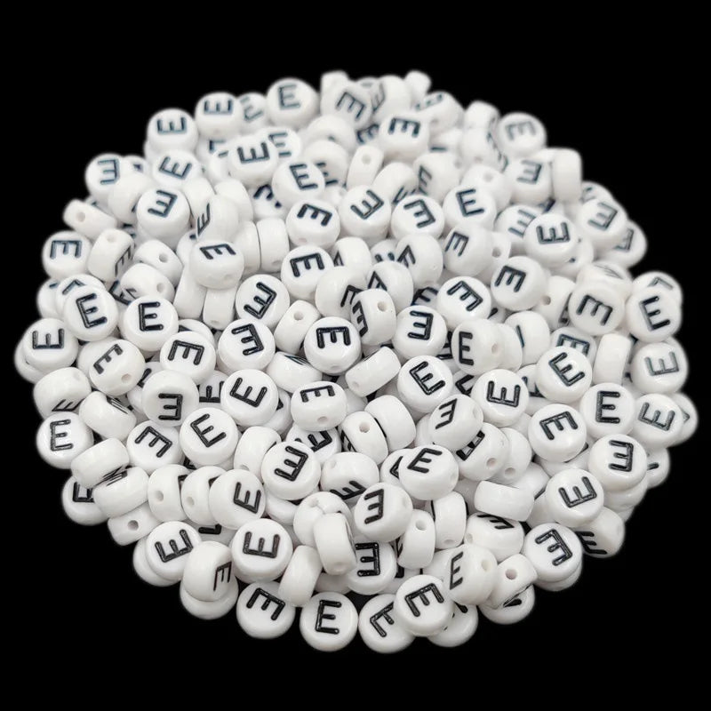 A pile of small white acrylic alphabet letter beads for jewelry making