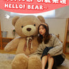 A young woman is sitting on a rug with a large brown teddy bear plush toy.