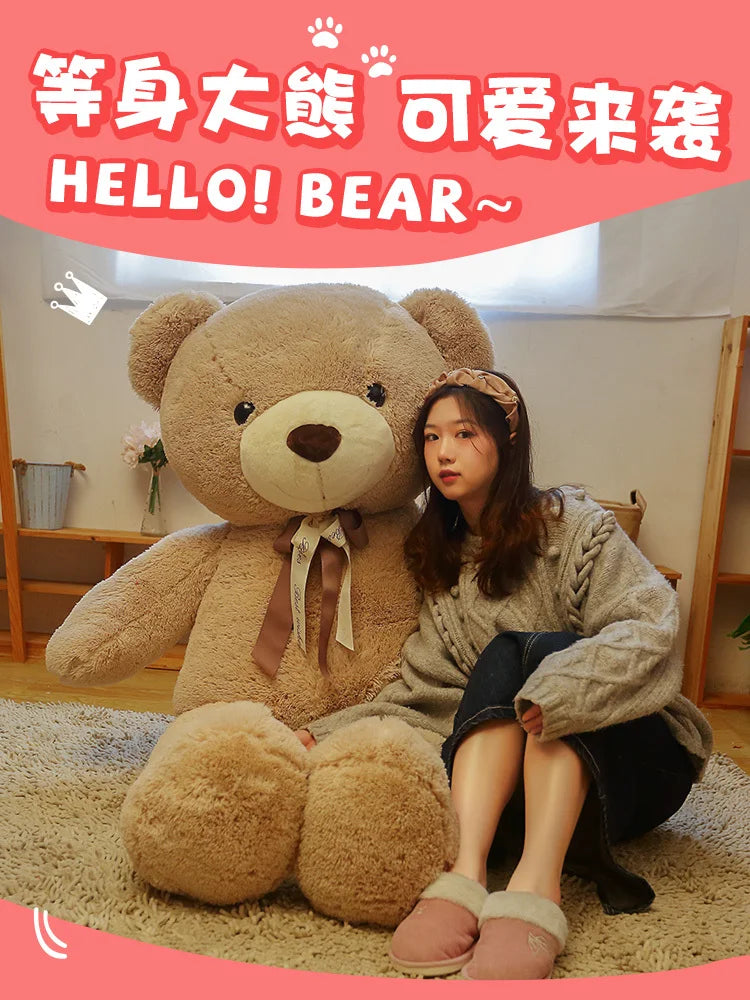 A young woman is sitting on a rug with a large brown teddy bear plush toy.