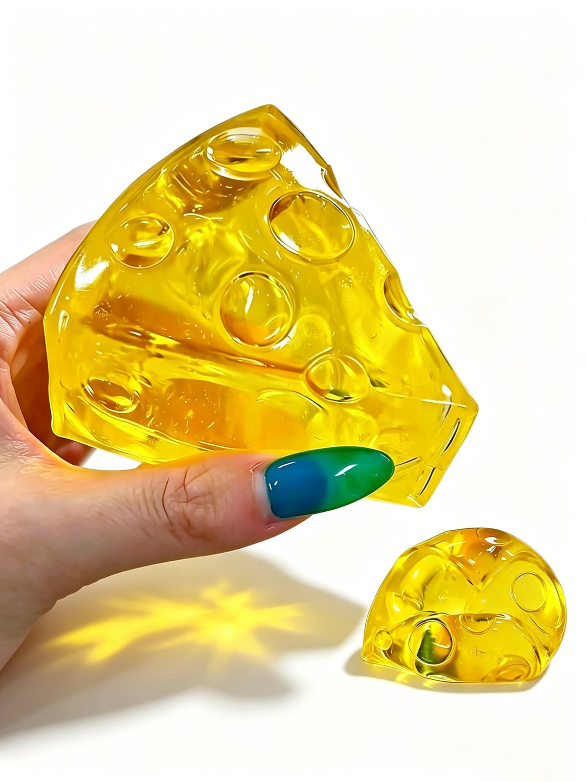 A hand holds a yellow, cheese-shaped squishy fidget toy with multiple holes against a white background.