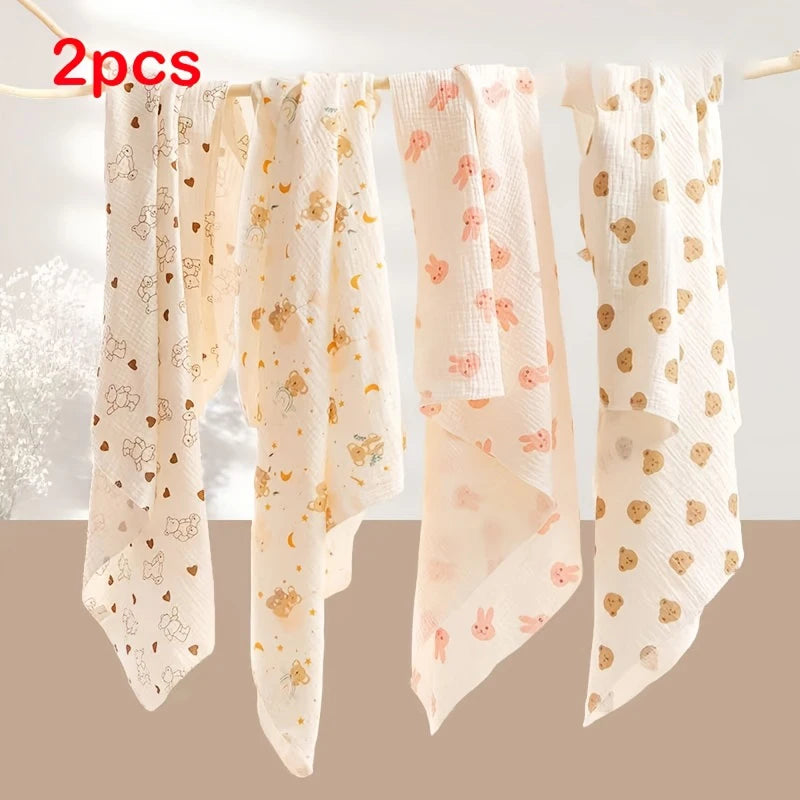 Two light pink baby gauze swaddle blankets with gold embroidered patterns hanging on a clothesline