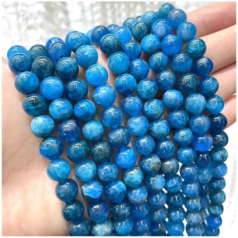 A hand holds a strand of small, round, blue-to-blue-green natural stone beads for jewelry making.