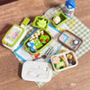 A set of miniature doll picnic lunch boxes in various colors and shapes, including a green box with food items and a white re