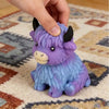 A purple and blue Scottish Highland cow stress relief squishy toy is being held by a hand on a rug.