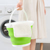 A person holds a white collapsible bucket with a green lid and handle, next to a washing machine.