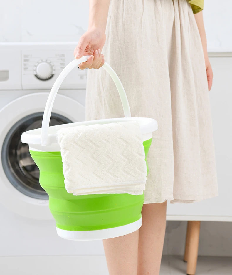 A person holds a white collapsible bucket with a green lid and handle, next to a washing machine.