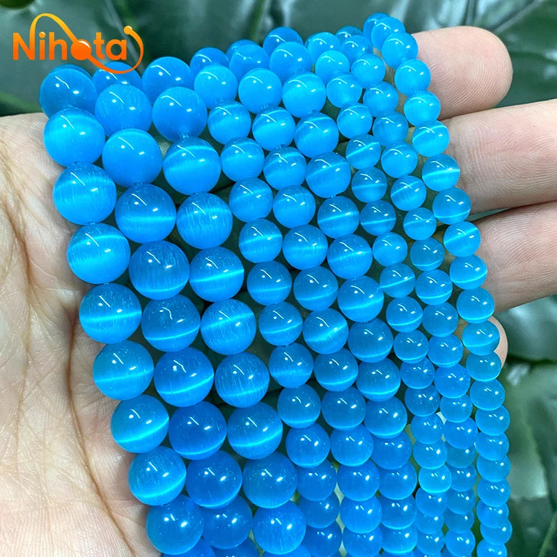 A hand holds a strand of bright blue cat eye stone beads for jewelry making