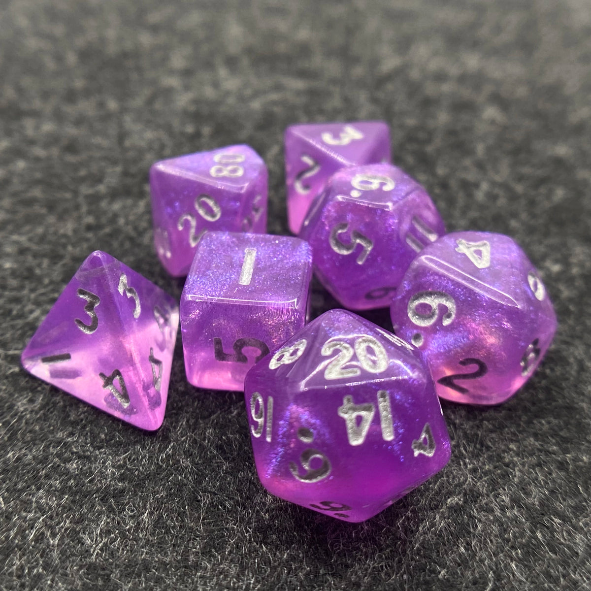 A pile of seven iridescent purple acrylic polyhedral dice resting on a dark, textured surface.