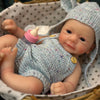 A hand-painted silicone reborn doll with an open mouth is nestled in a woven basket lined with fabric.