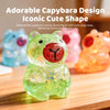 A transparent, glittery green capybara squishy toy sitting on a wooden surface.