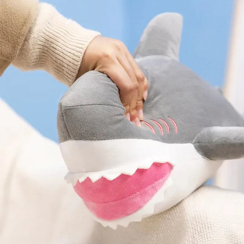 A hand is holding a gray and pink plush stuffed animal shaped like a killer whale and great white shark.