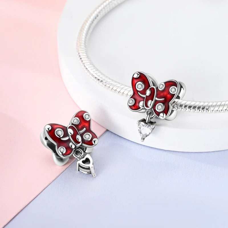 A sterling silver butterfly charm with red enamel and clear stones is displayed on a white background.