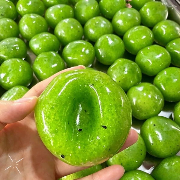 A hand holds a bright green kiwi slush squishy fidget toy surrounded by many similar toys.
