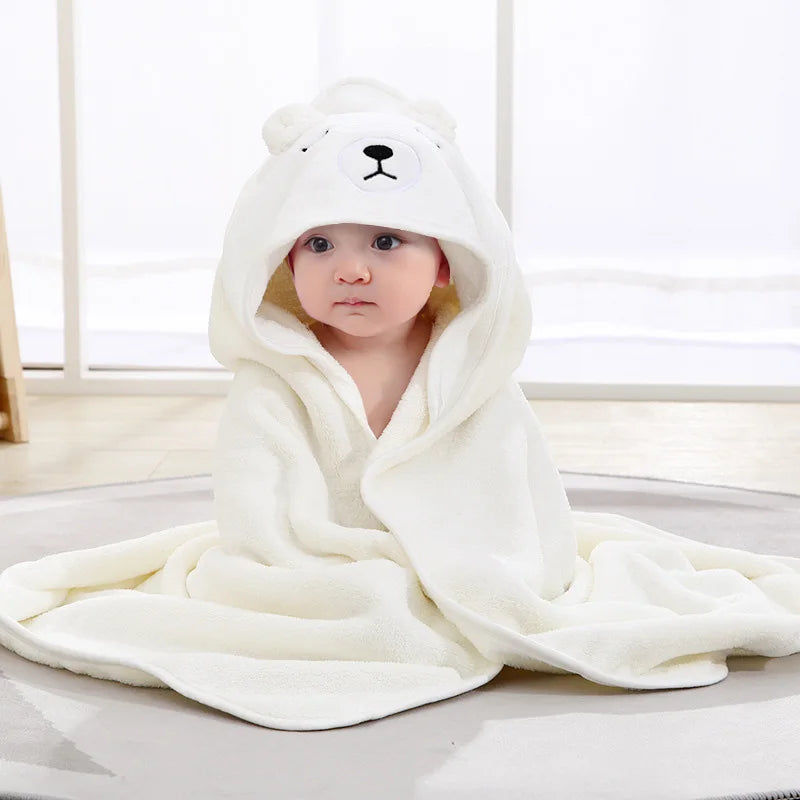A baby wearing a white hooded animal bath towel, likely a bear design, is shown indoors.