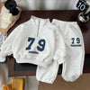 A gray kids' 2-piece set featuring a long-sleeve sweater and sweatpants with the number 79 printed on them.