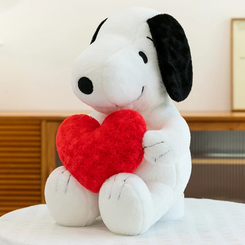 A white plush toy resembling Snoopy with black ears, holding a red heart, sitting on a white surface.