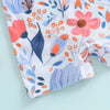 A close-up of a white baby rash guard swimsuit with a floral print featuring pink, orange, and blue leaves and flowers.