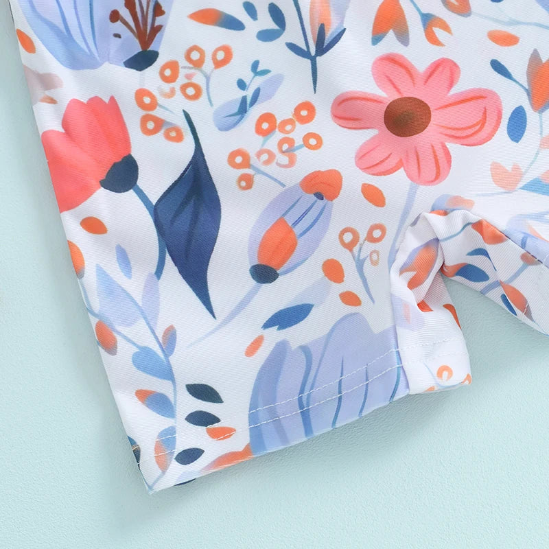A close-up of a white baby rash guard swimsuit with a floral print featuring pink, orange, and blue leaves and flowers.