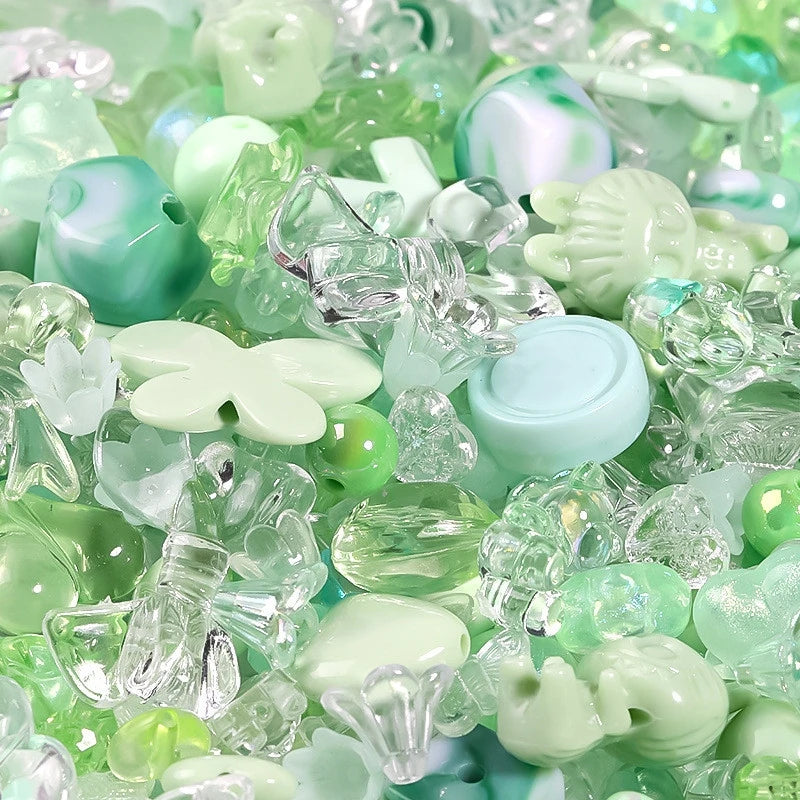 A close-up of mixed clear and light green acrylic loose beads for jewelry making.