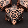 A close-up of a bronze metal dice set featuring three-sided dice with engraved numbers, resting on a dark surface.