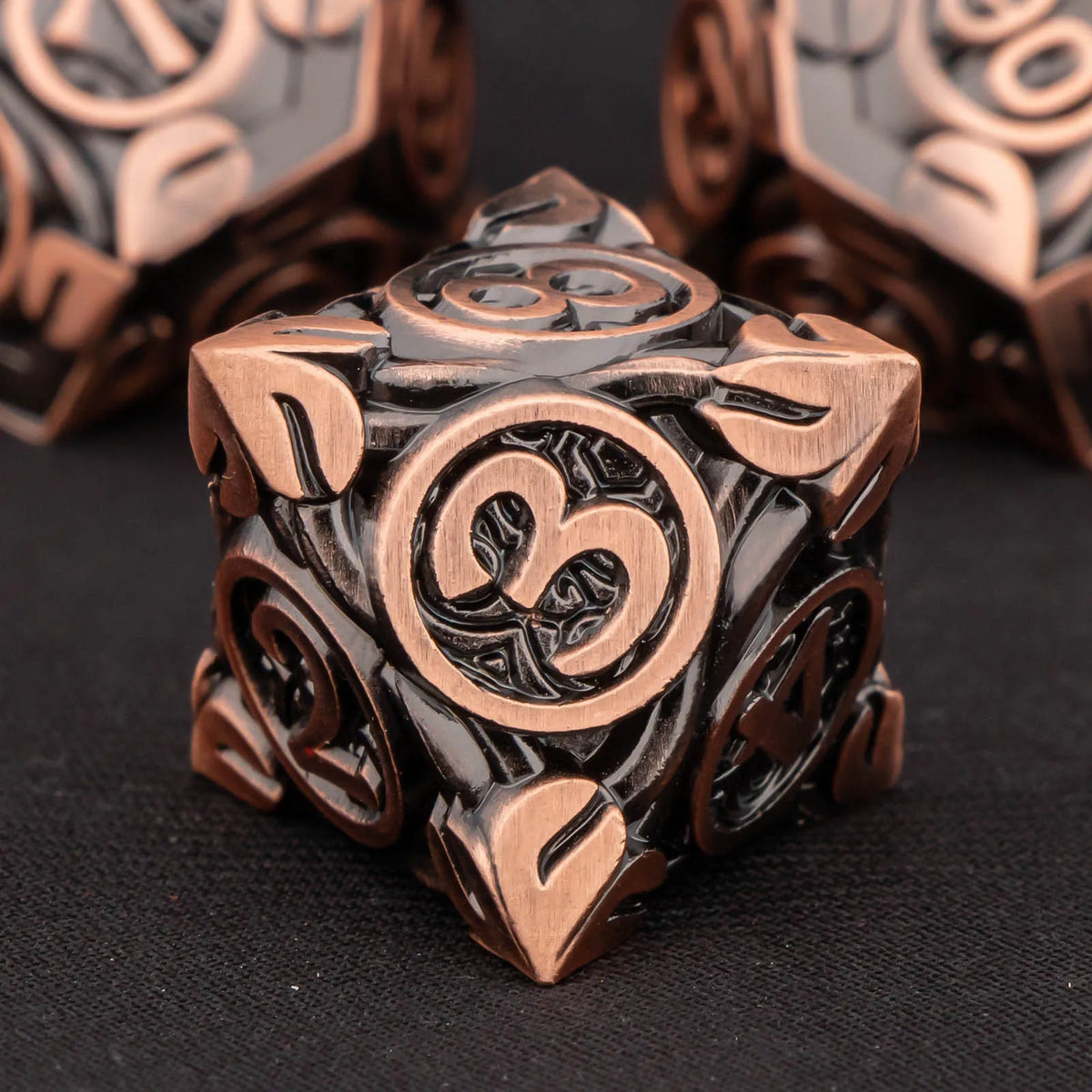 A close-up of a bronze metal dice set featuring three-sided dice carved into a geometric shape.
