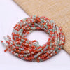 A strand of faceted crystal rondelle beads in shades of pink, orange, and green is coiled on a beige fabric.