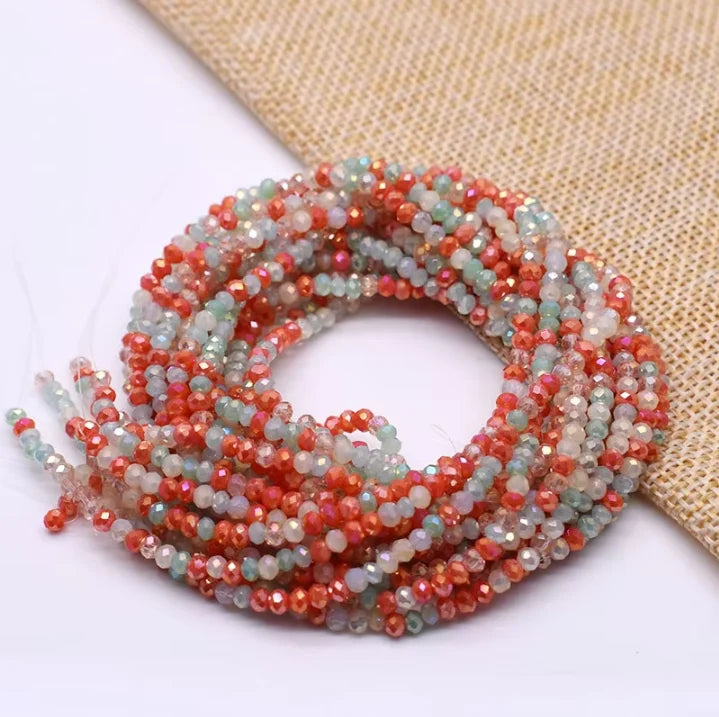 A strand of faceted crystal rondelle beads in shades of pink, orange, and green is coiled on a beige fabric.